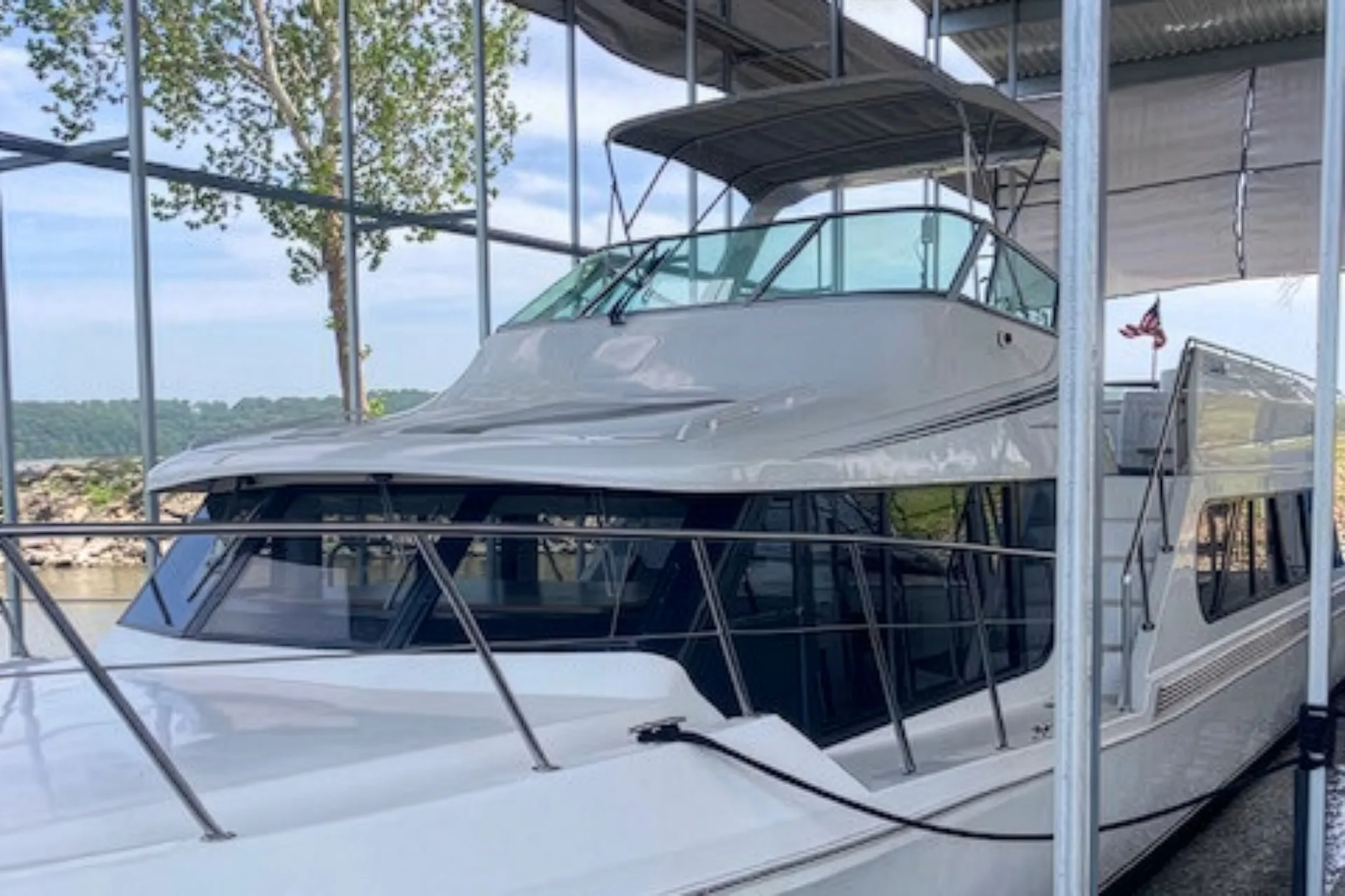 White yacht docked in a covered marina with surrounding metal poles and an American flag.