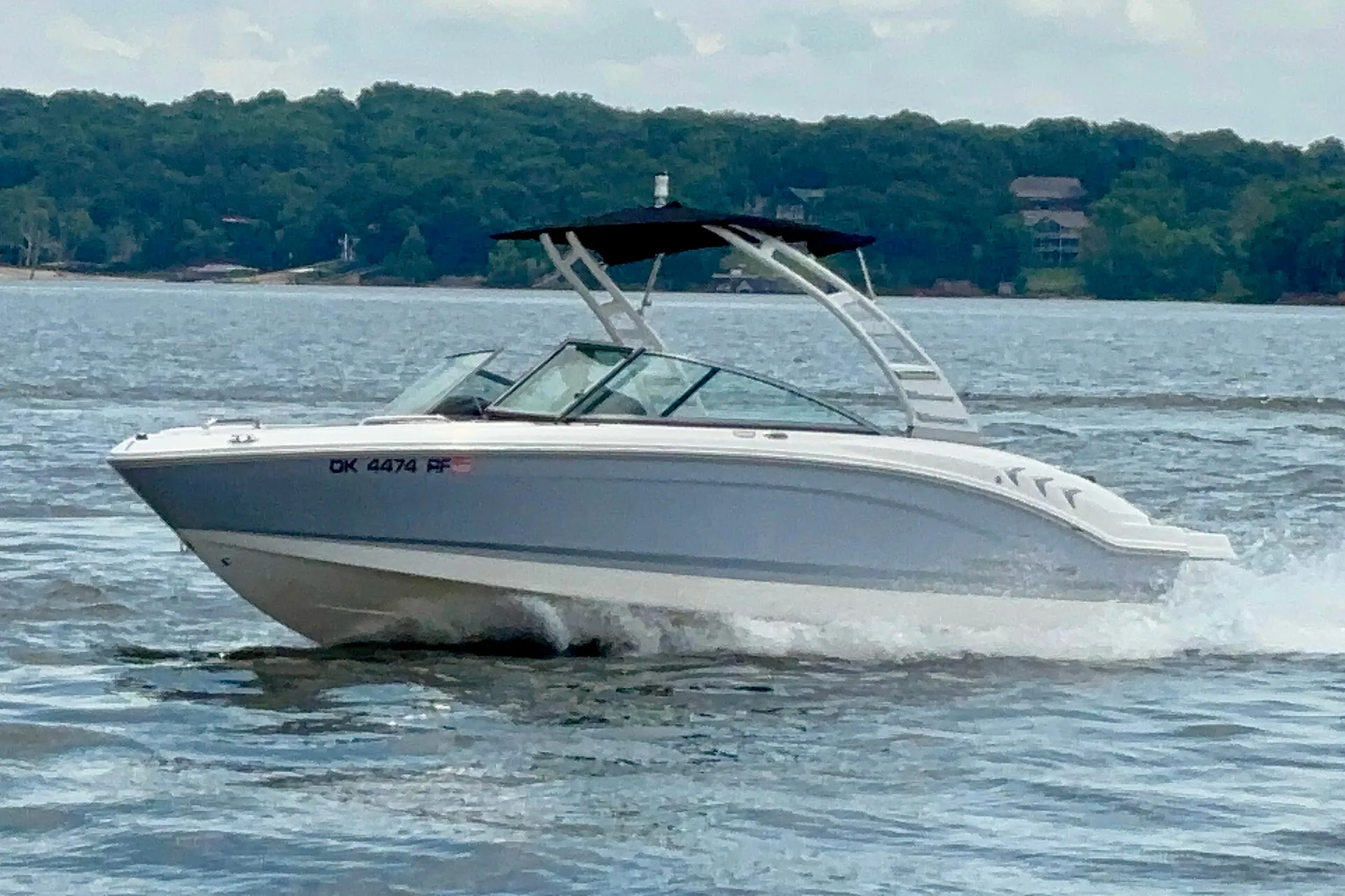 White and gray motorboat with black canopy cruising on a lake with a forested shore in the background.