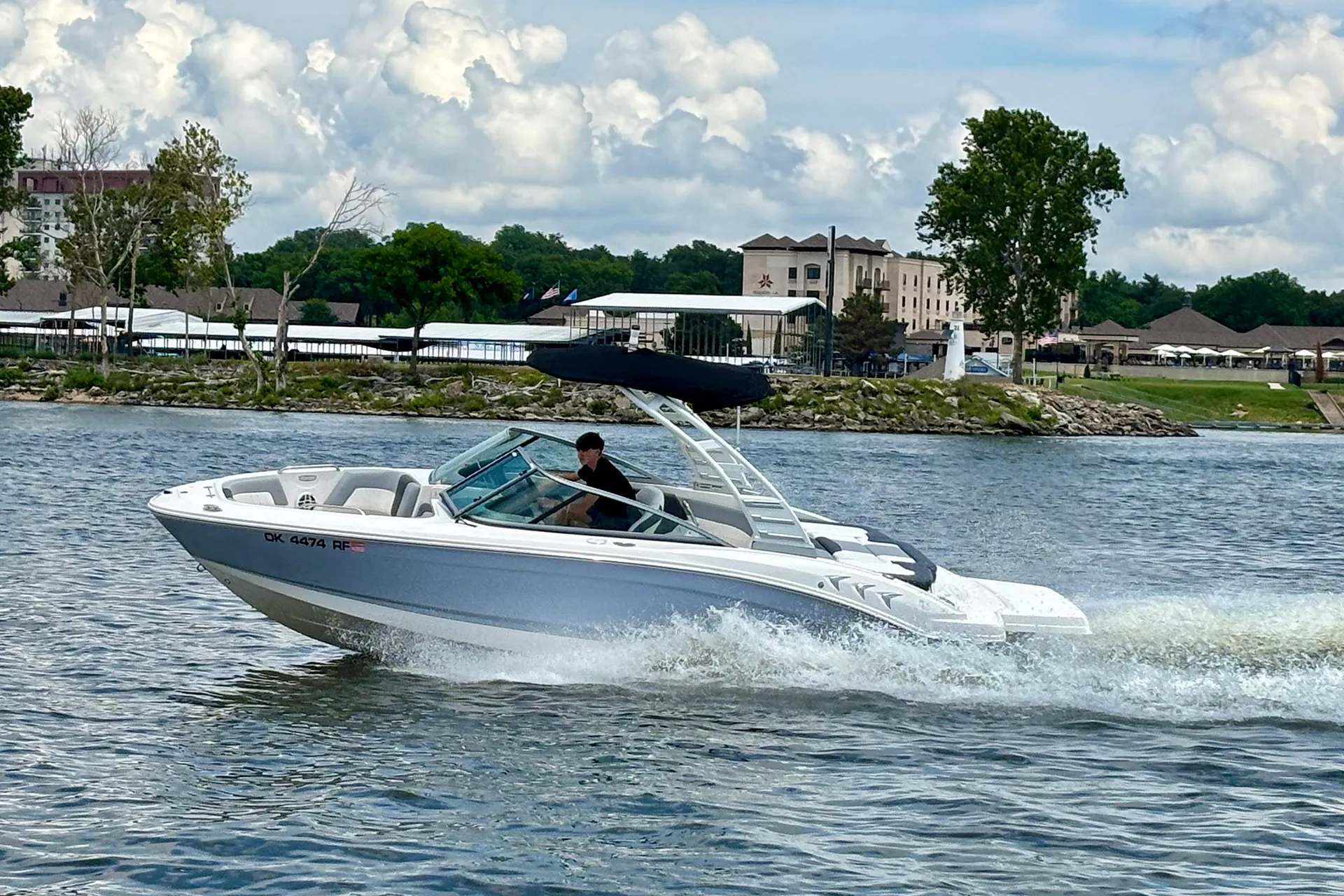 White motorboat with T-top speeding on lake with buildings and trees in the background.