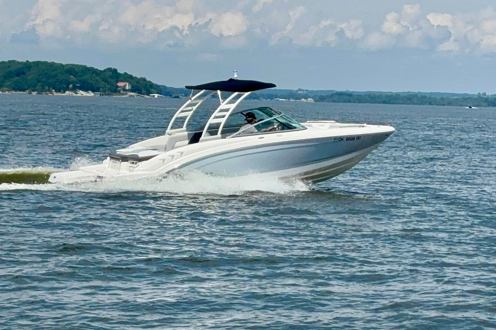 White speedboat with black canopy moving fast on a large body of water under a cloudy sky.