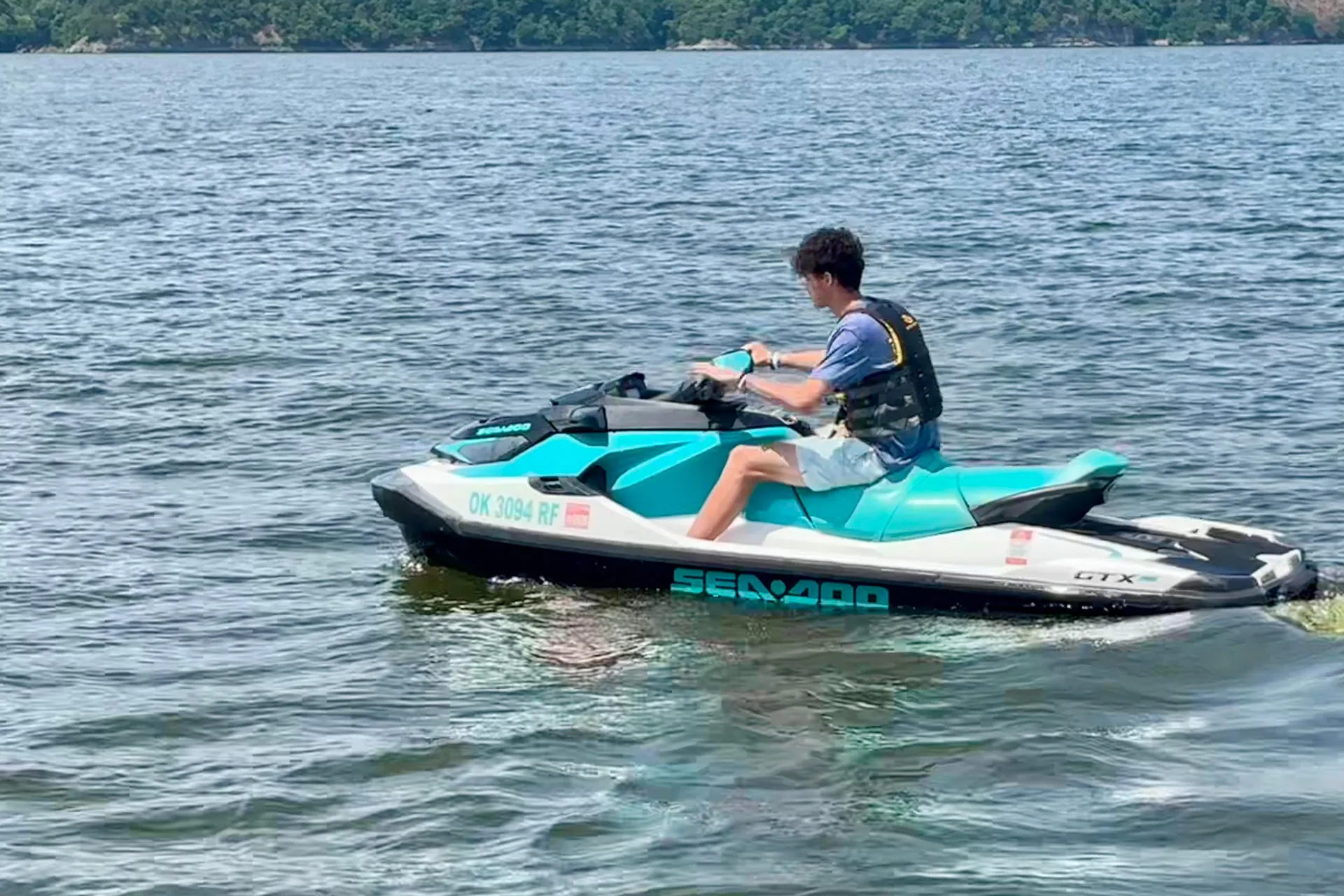 Person wearing life jacket riding a turquoise and white Sea-Doo jet ski on a lake.