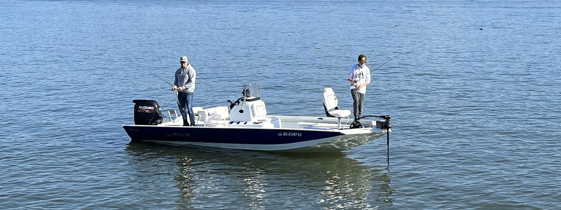 Two people fishing on a small blue and white motorboat on calm water.