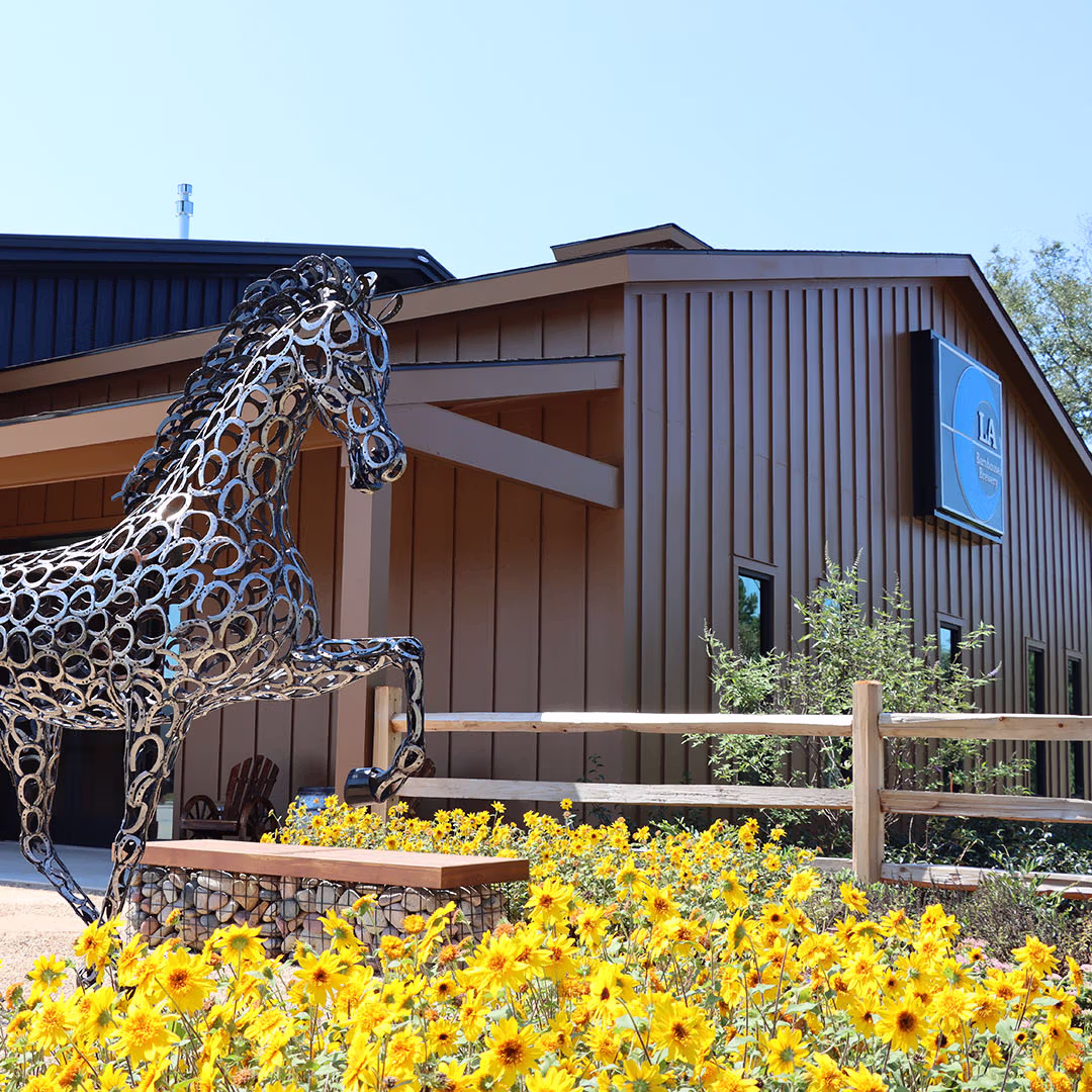 Decorative metal horse sculpture at LA Barnhouse Brewery in Ponchatoula, Louisiana, set among vibrant wildflowers and rustic barn-inspired architecture, reflecting the brewery’s connection to nature, creativity, and community.