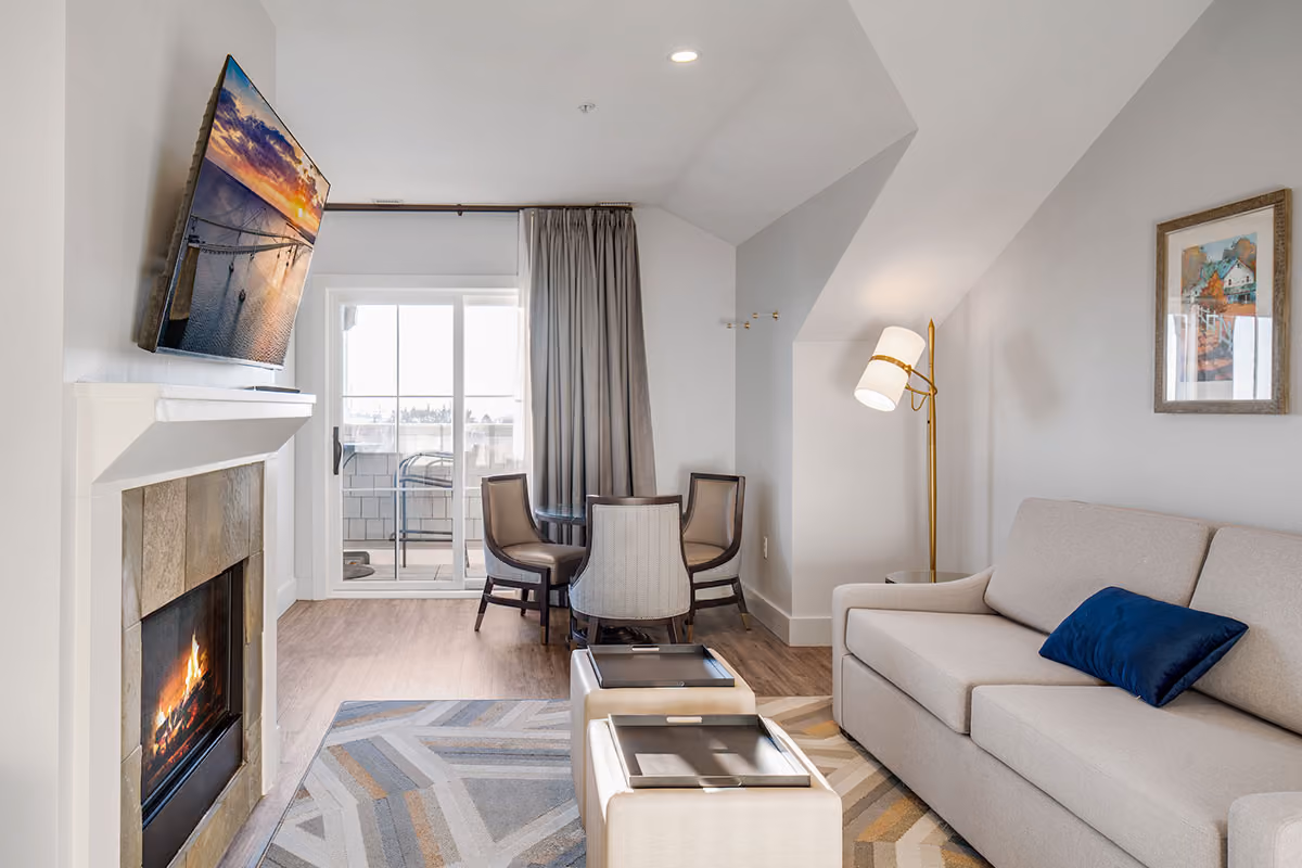 Modern living room with a sofa, fireplace, wall-mounted TV, round dining table, and sliding glass doors to a balcony.