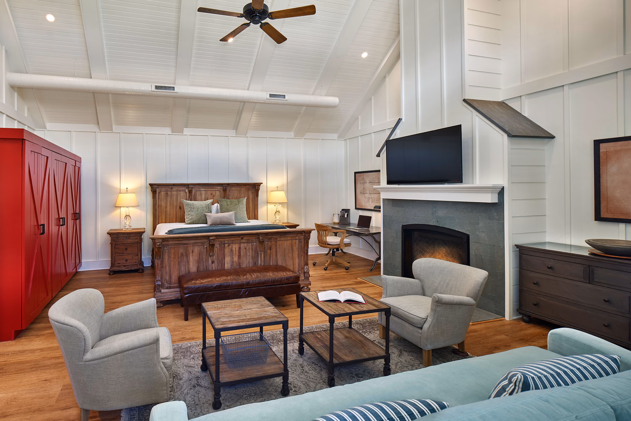 Spacious bedroom with a wooden bed, sitting area, fireplace, TV, red wardrobe, and vaulted ceiling with a ceiling fan.