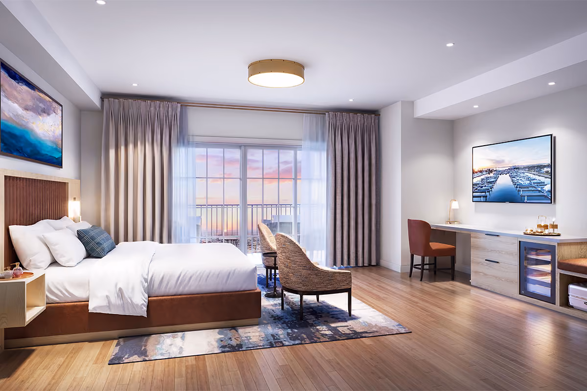 Modern hotel room with a large bed, two chairs, desk, and balcony overlooking a sunset view through sliding glass doors.