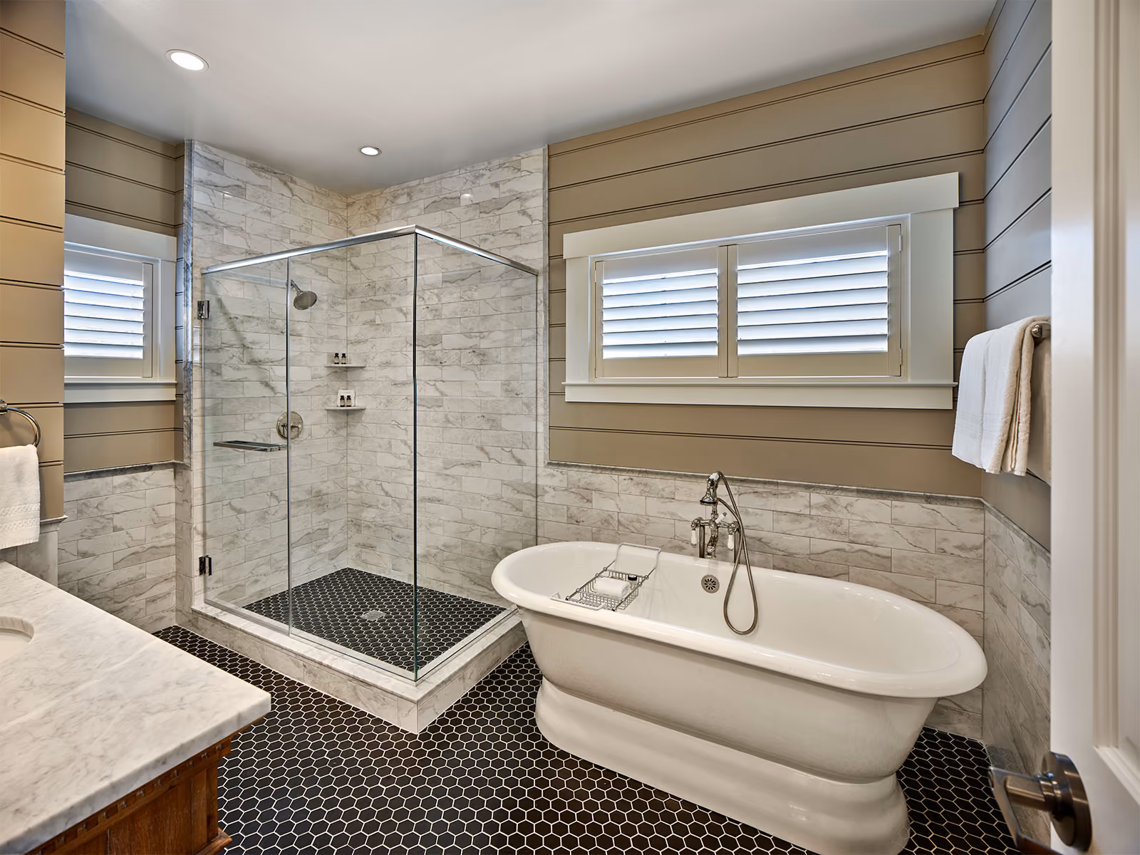 Modern bathroom with a glass shower, freestanding bathtub, marble accents, and hexagonal floor tiles.