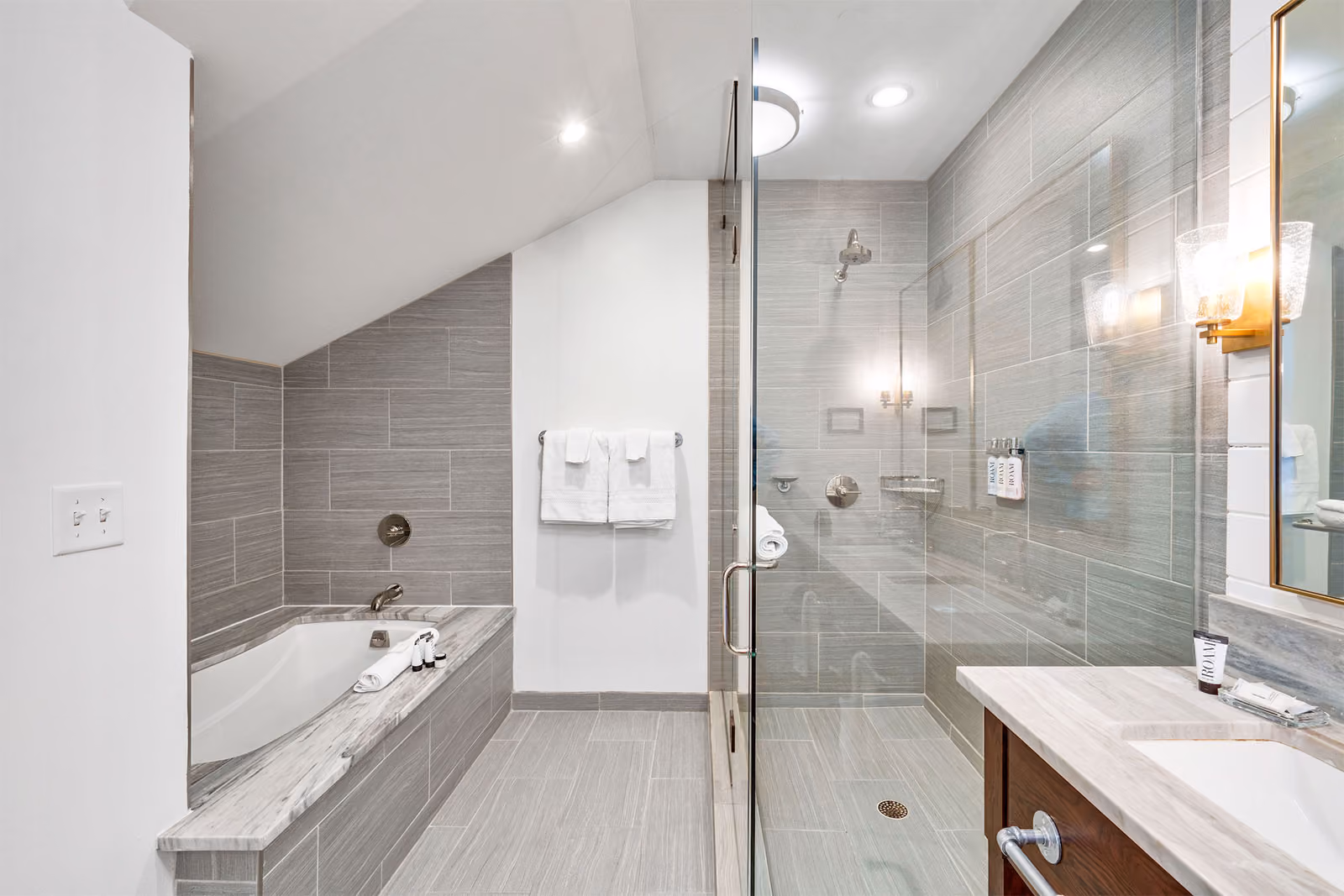 Modern bathroom with a bathtub, glass-enclosed shower, wall-mounted towel rack, and large mirror above the sink.