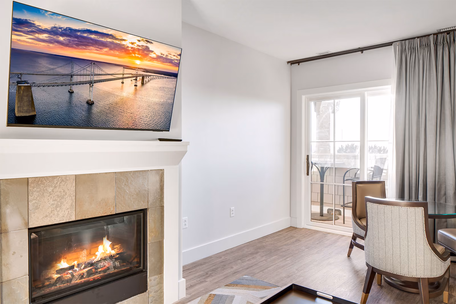 A modern living room with a fireplace, wall-mounted TV, dining area, and a sliding door to a balcony.