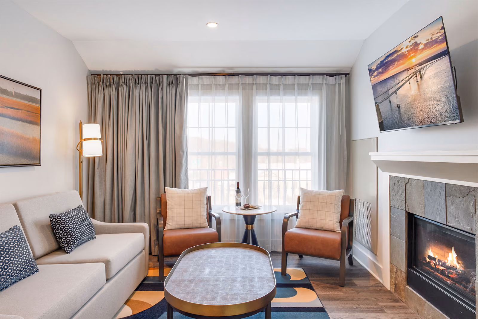 Modern living room with a sofa, two chairs, a coffee table, a wall-mounted TV, and large windows with curtains.