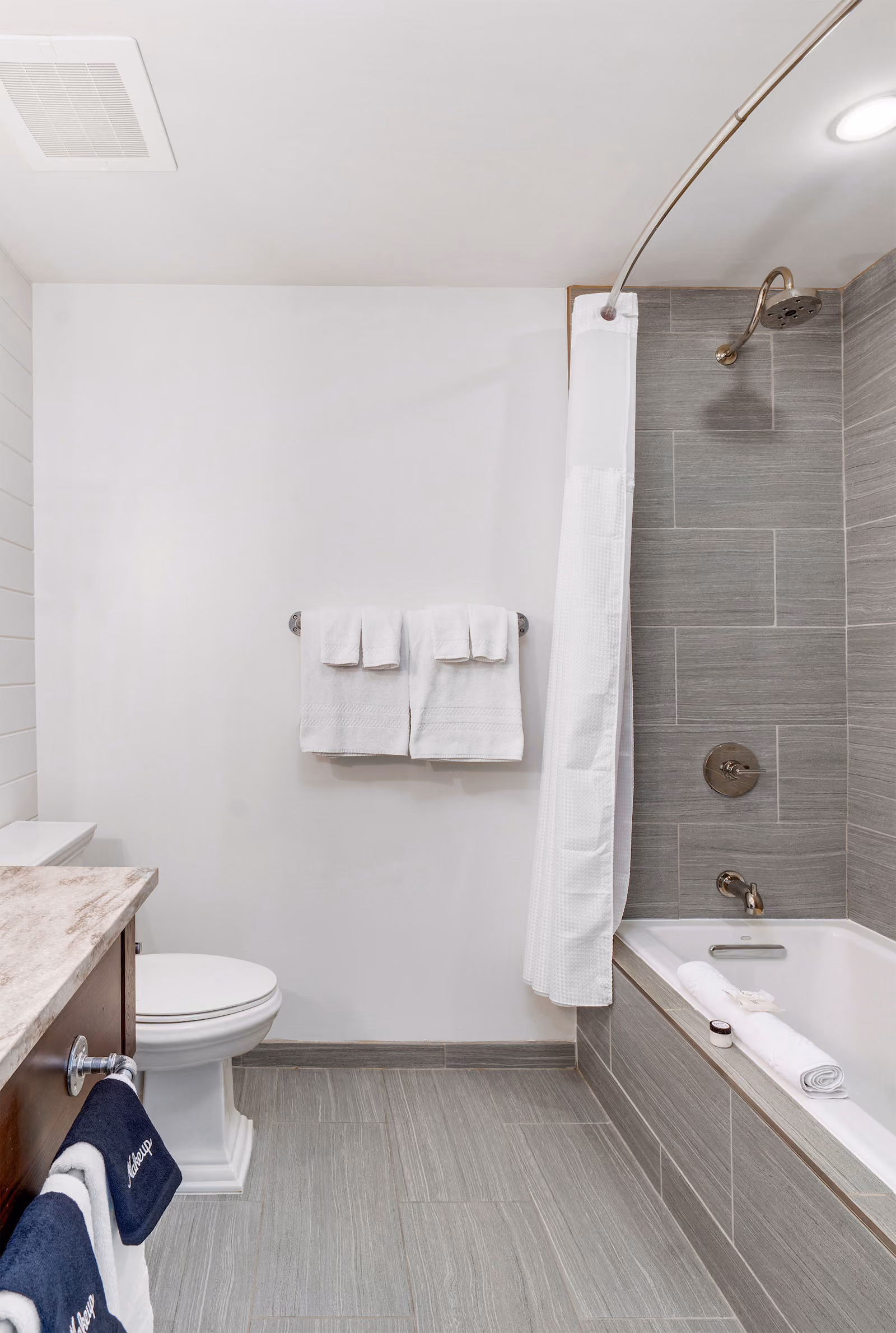 Modern bathroom with a bathtub, shower, toilet, vanity, and neatly folded white towels on racks.