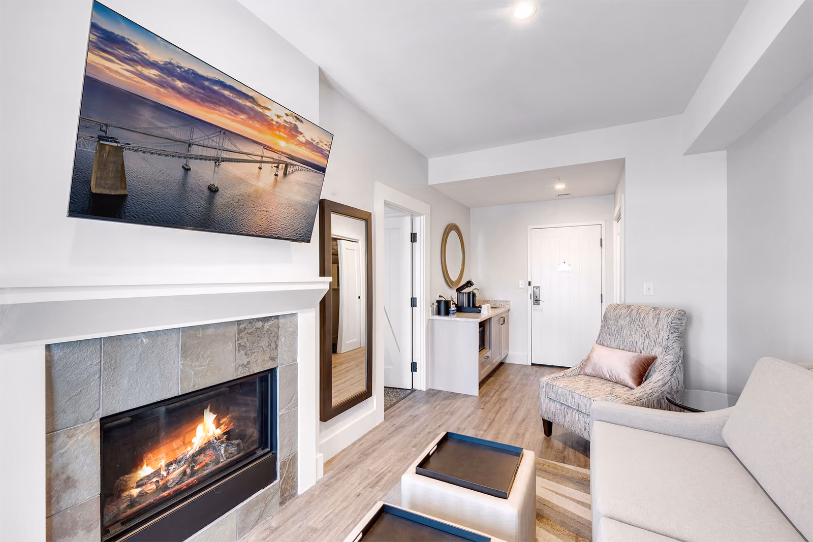 Modern living room with a fireplace, wall-mounted TV, armchair, sofa, and a small kitchenette near the entrance.