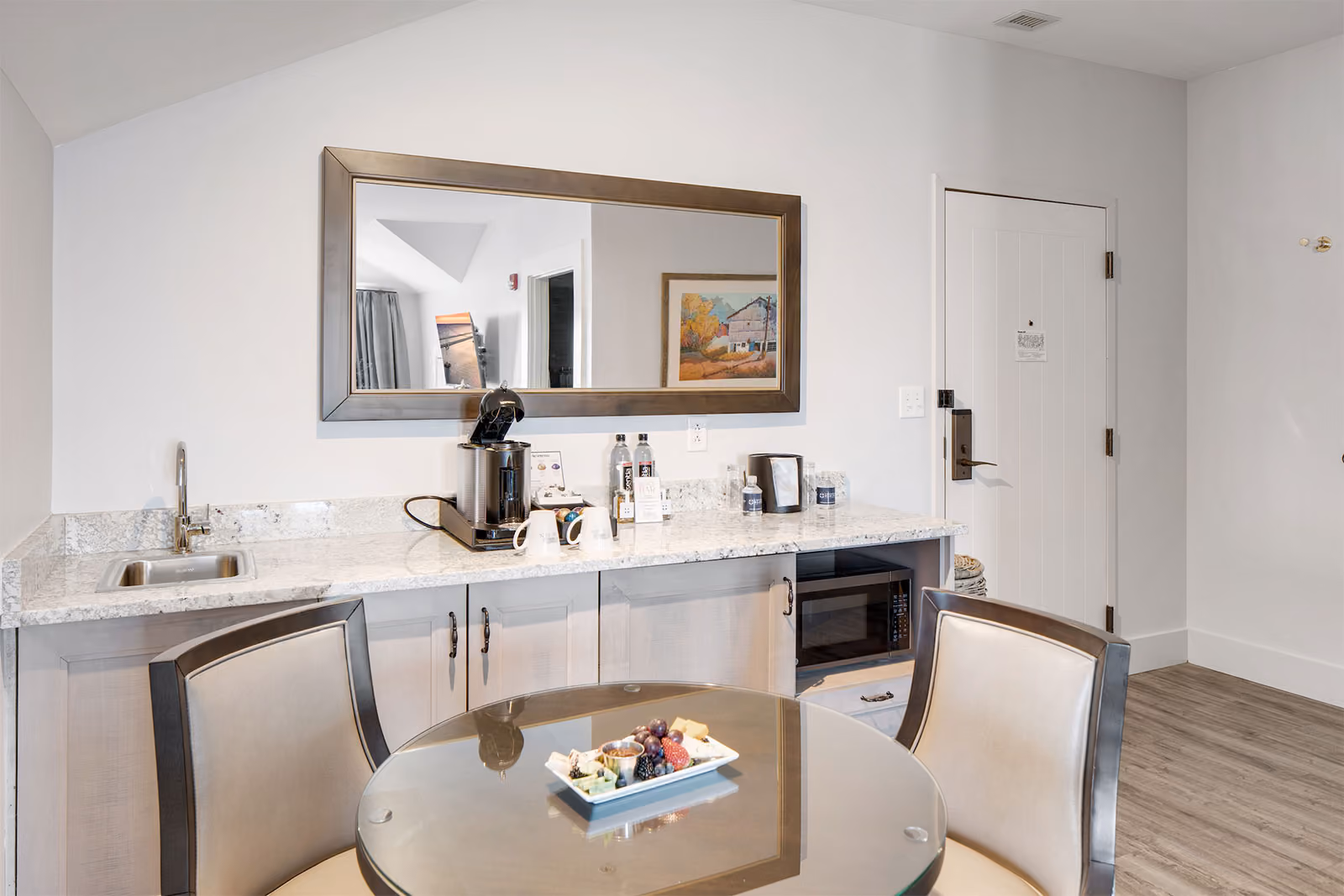 Kitchenette with a sink, coffee maker, microwave, and a round glass table with chairs and a plate of fruit.