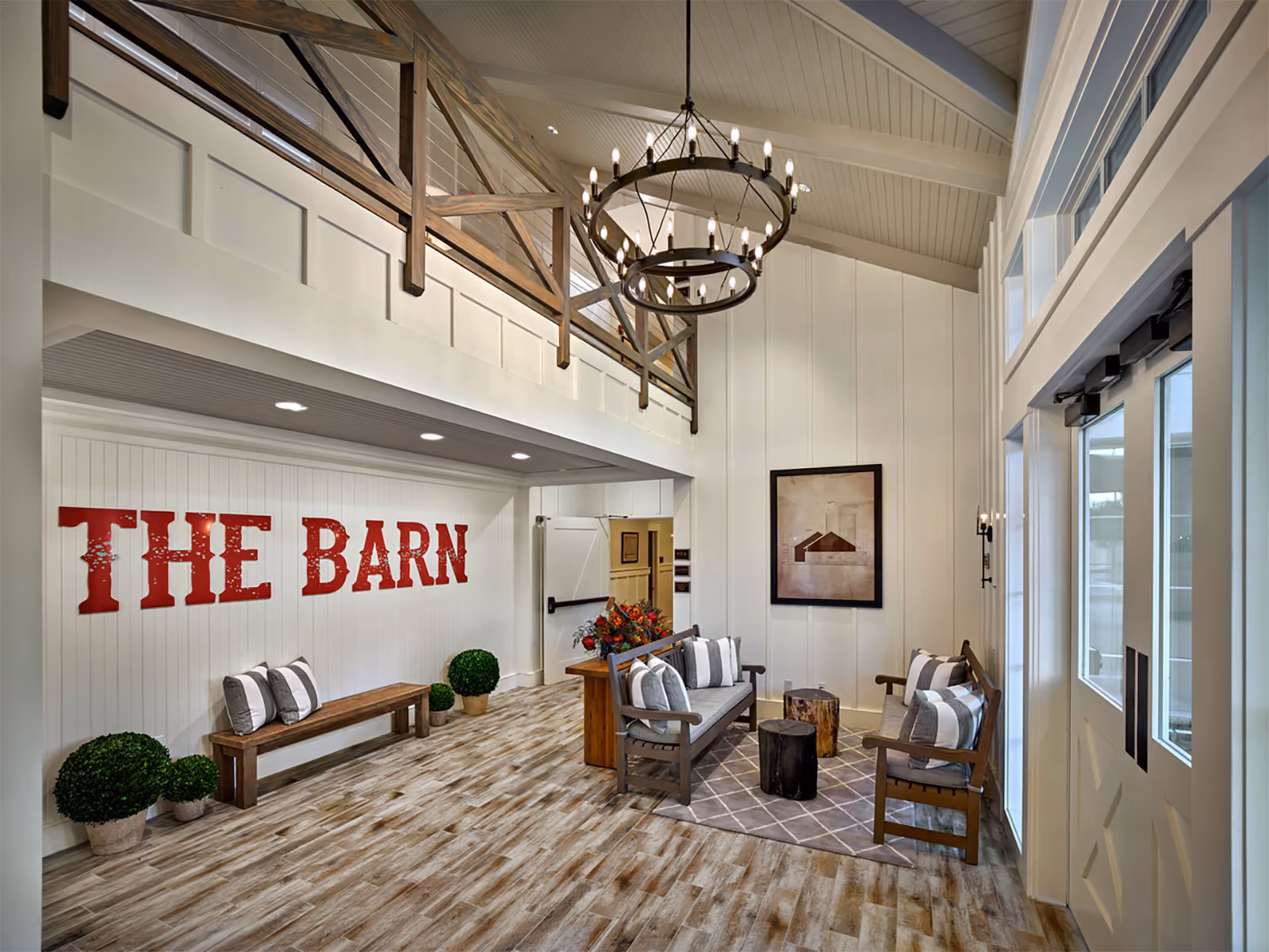 Lobby area with wood beams, benches, and "The Barn" sign on wall; modern rustic decor and chandelier overhead.