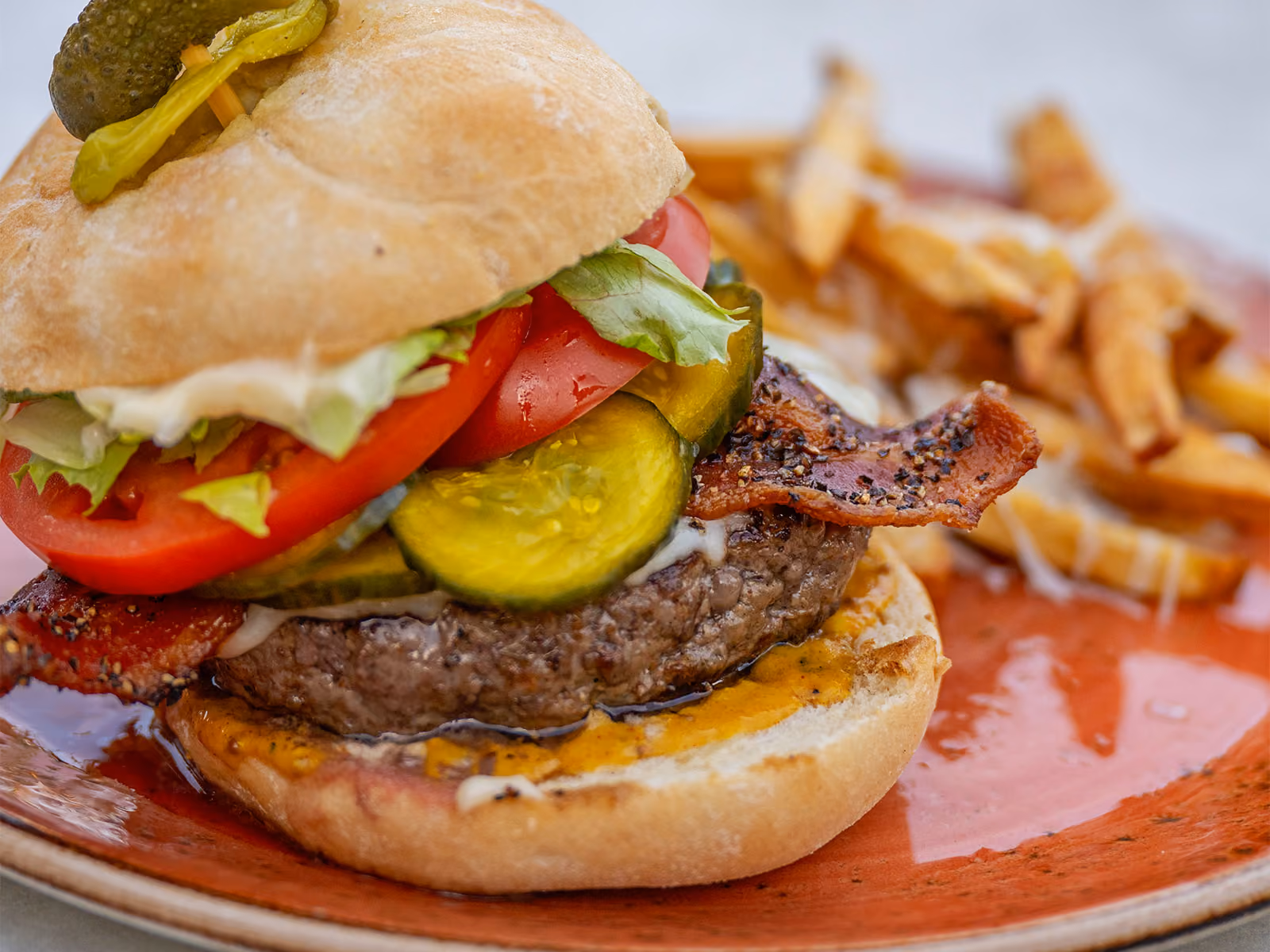 Loaded burger with bacon, tomato, pickles and lettuce served with fries on a red plate