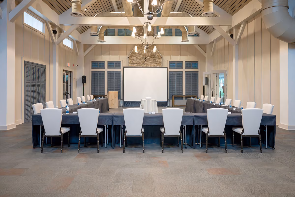 Conference room with U-shaped table setup, white chairs, a projector screen, and modern ceiling fixtures.