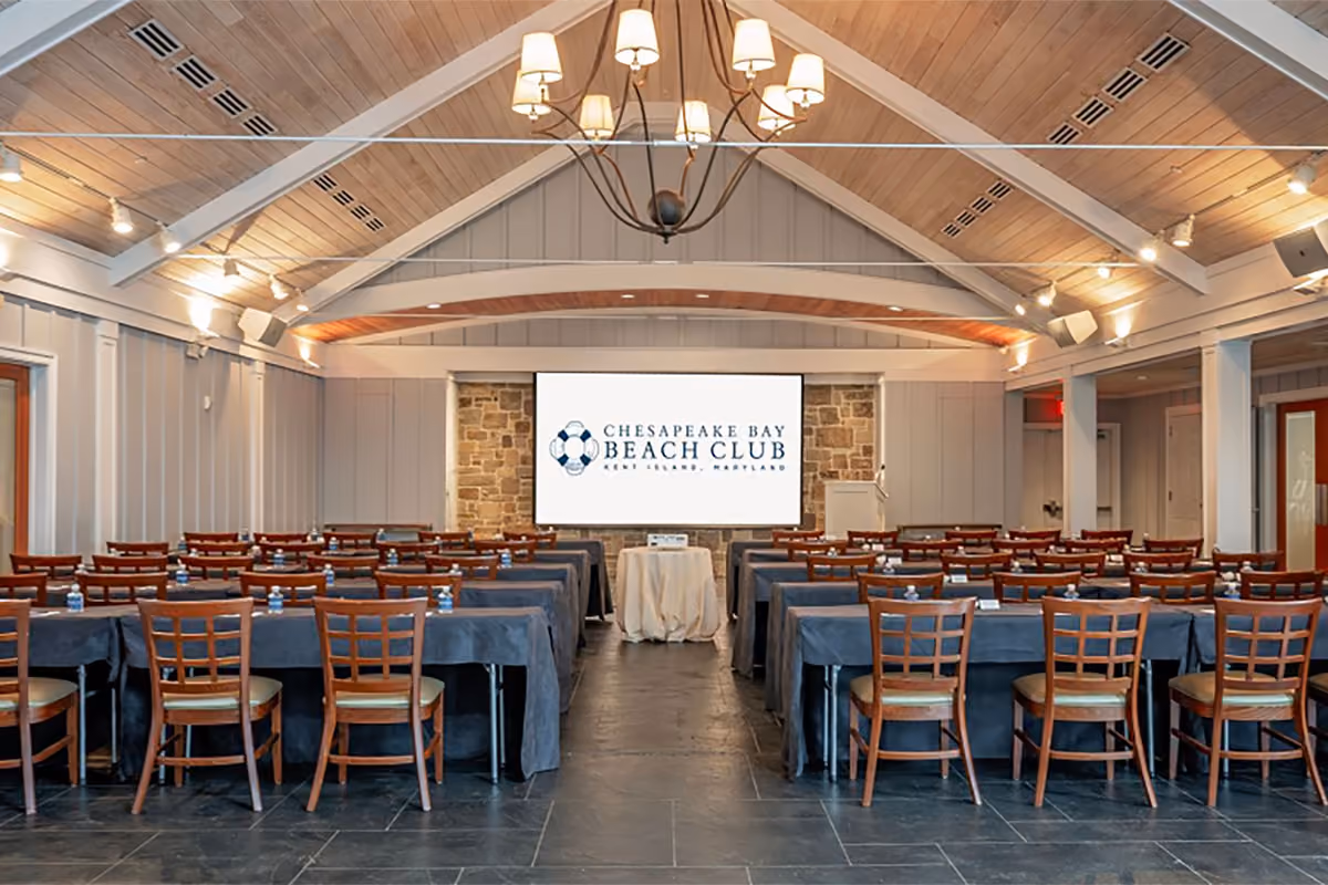 Conference room set up with rows of tables and chairs facing a projection screen at Chesapeake Bay Beach Club.