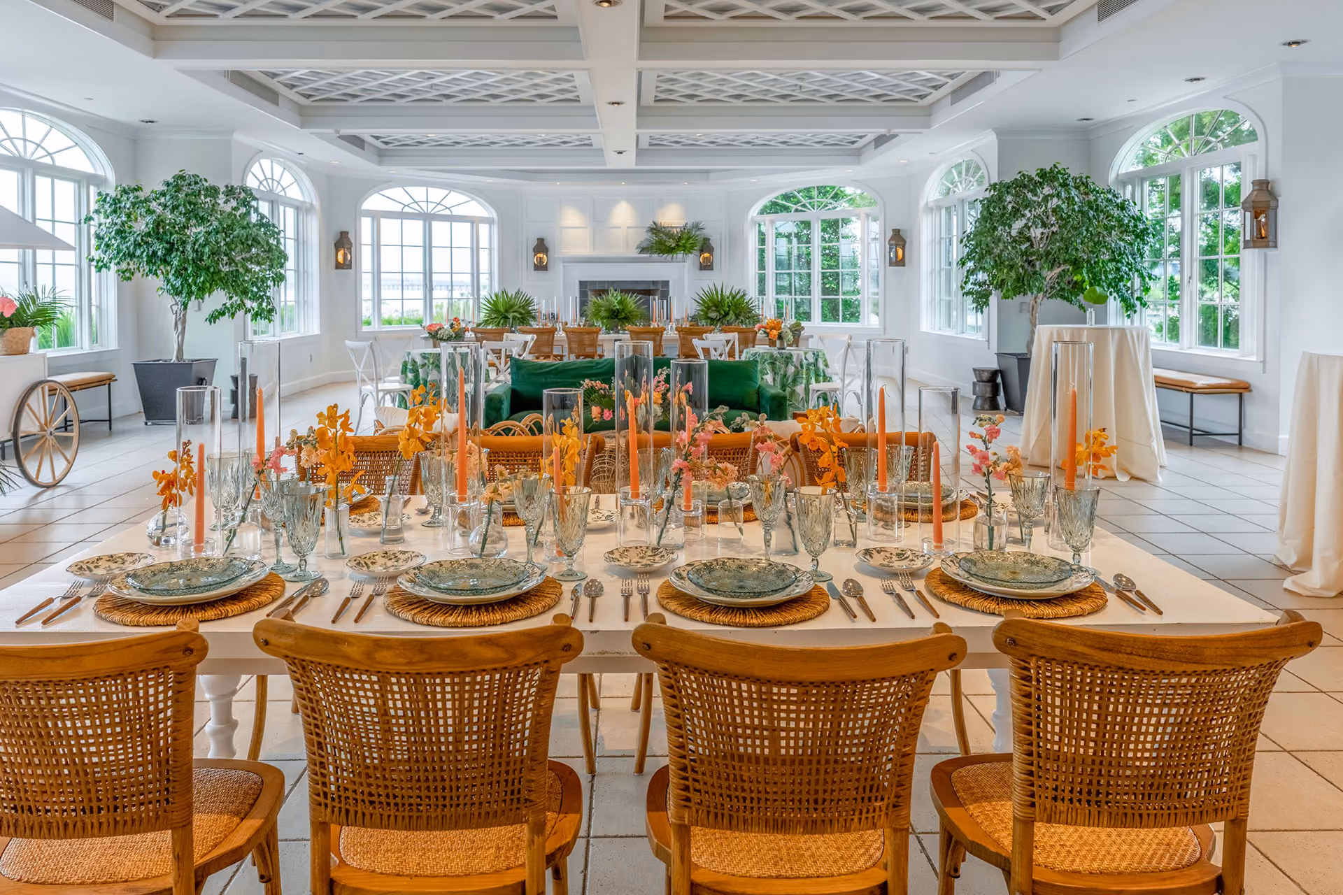 Elegant dining table set with plates, glasses, and orange candles in a bright, spacious room with greenery and large windows.