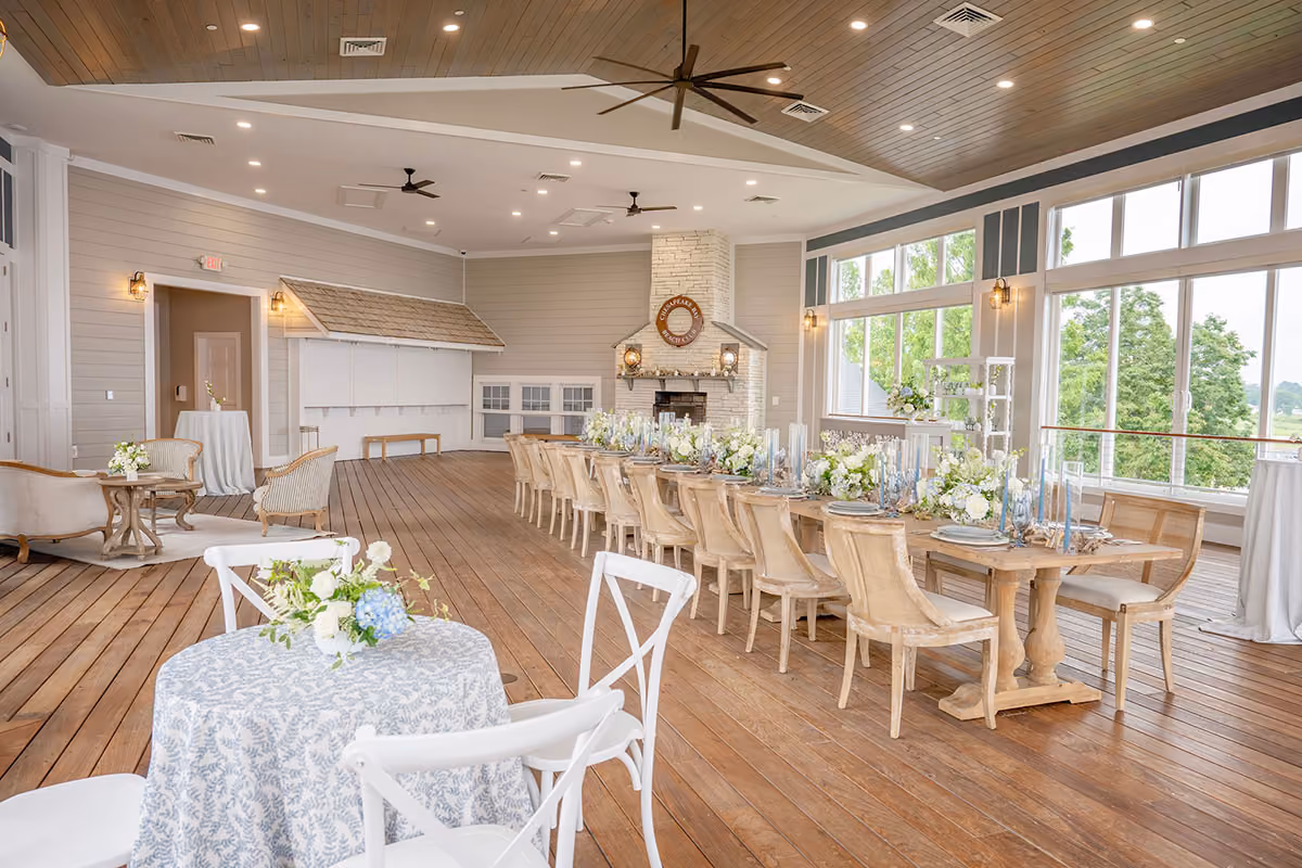 A bright event space with large windows, wooden floors, and a long dining table set for a formal gathering.