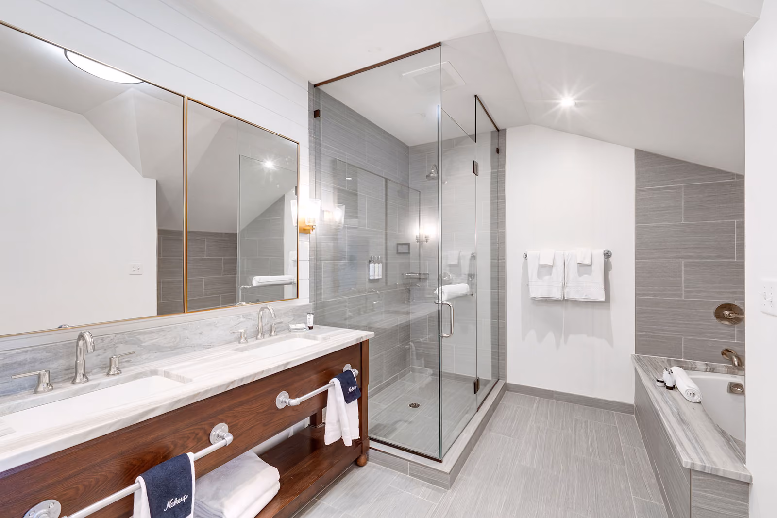 Modern bathroom with double sink vanity, glass-enclosed shower, bathtub, and gray tile walls and floor.
