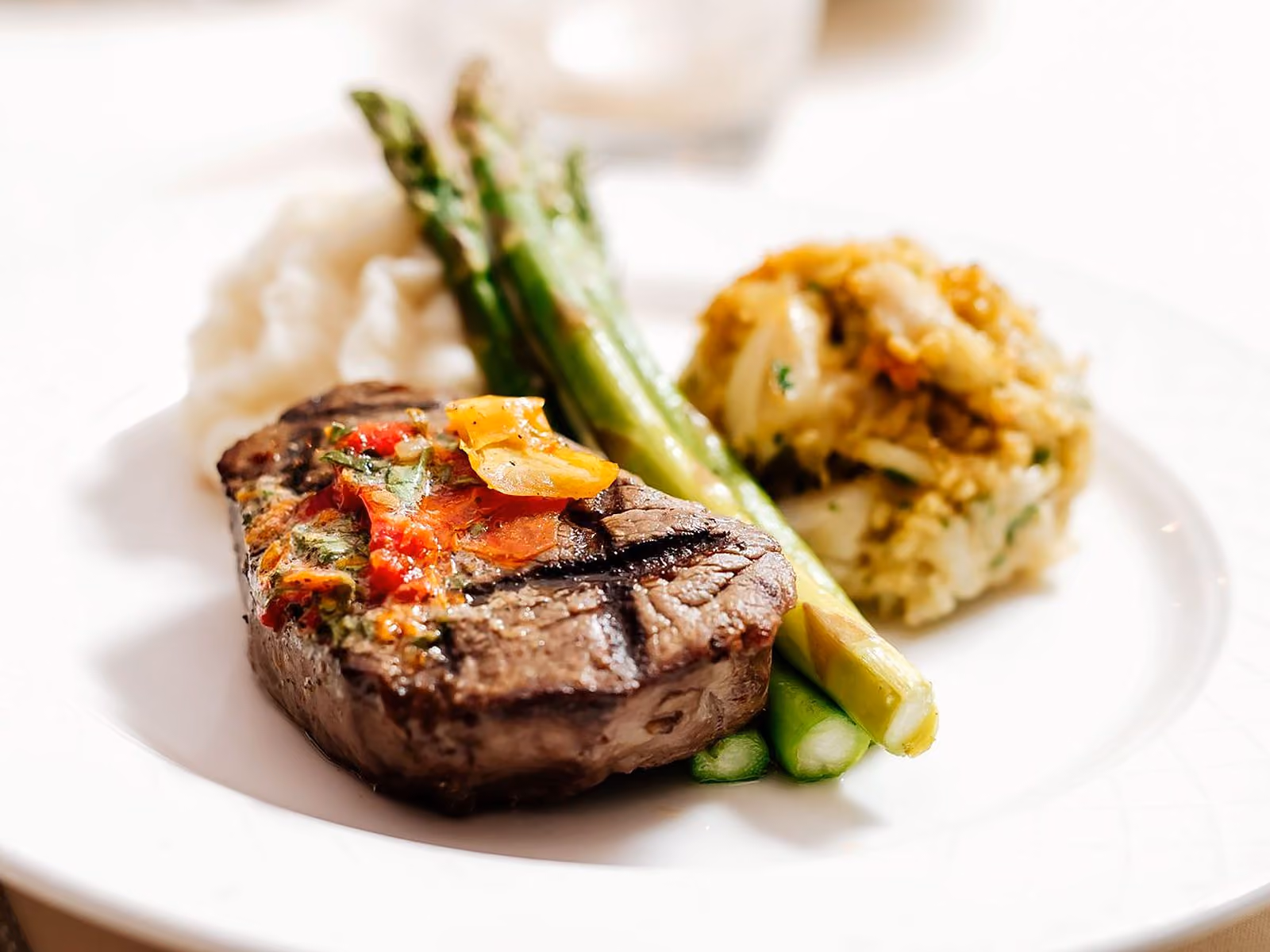 Plated wedding dinner of grilled filet, grilled asparagus, mashed potatoes and crab on a white plate