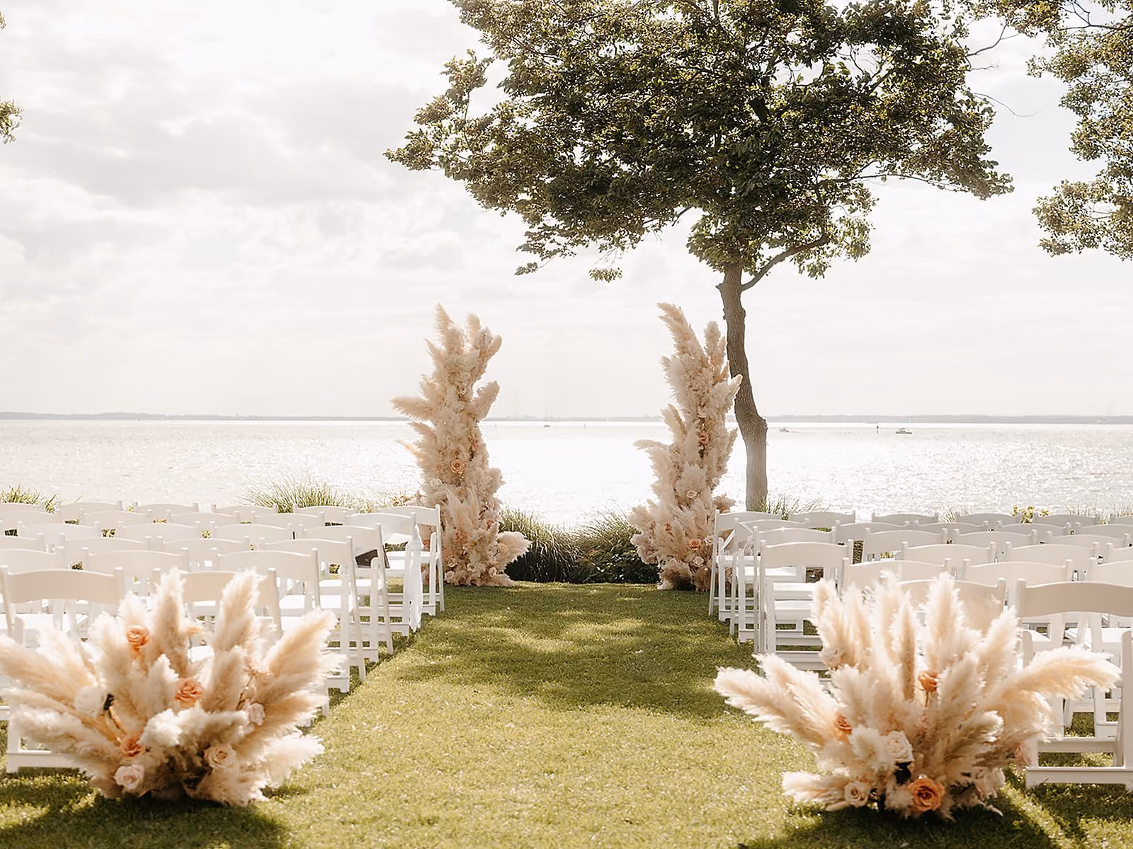 Outdoor waterfront wedding ceremony with pampas grass florals and white chairs overlooking Chesapeake Bay