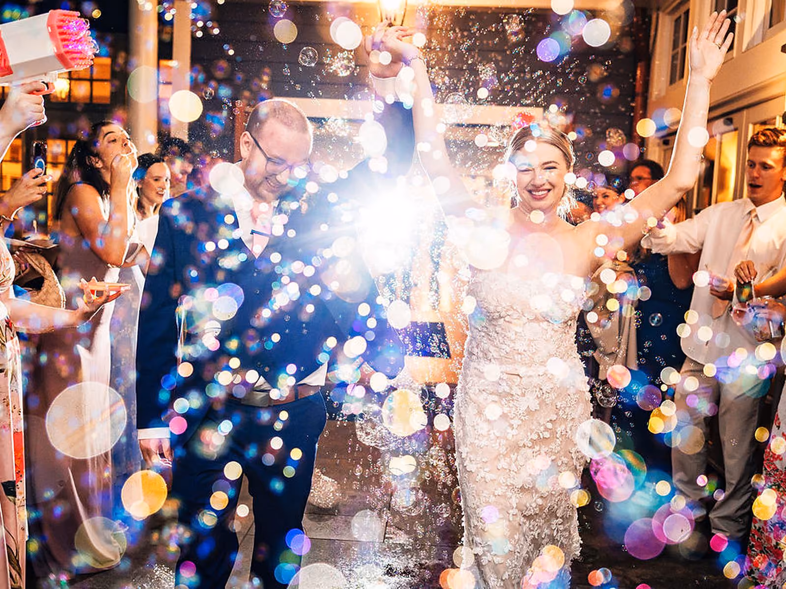 Bride and groom celebrating during a sparkling bubble send-off as guests cheer at their evening wedding exit