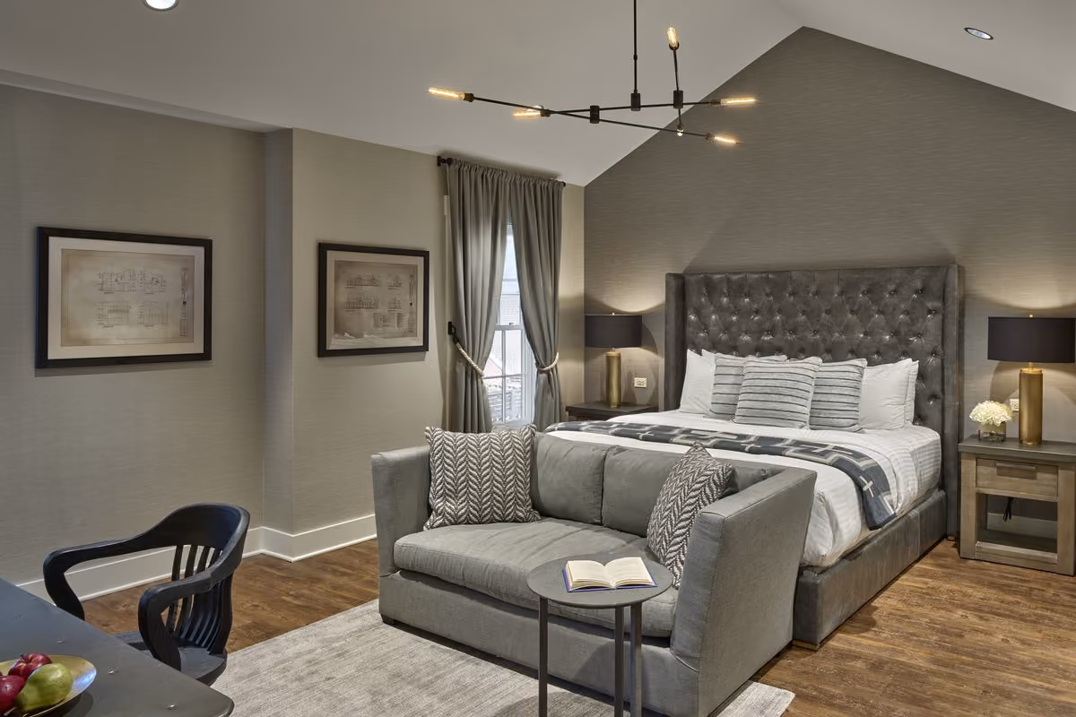 Spacious king guest room with a tufted gray headboard, sitting-area sofa and vaulted ceiling at Chesapeake Bay Beach Club