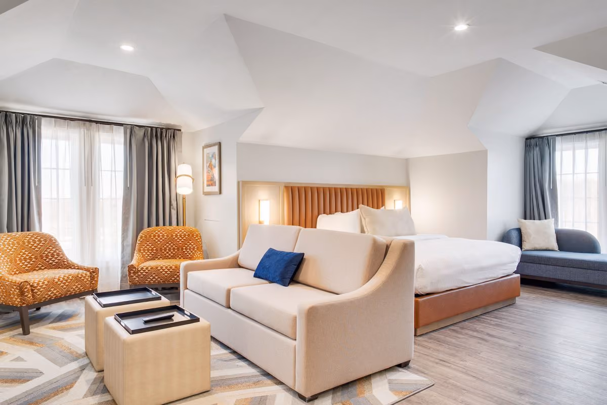 Spacious modern king suite with a sofa, two orange accent chairs and a bright sitting area