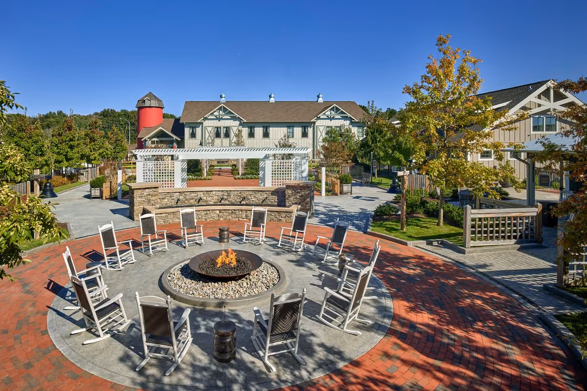 Outdoor courtyard with a circular fire pit ringed by white rocking chairs and a brick patio beside the inn