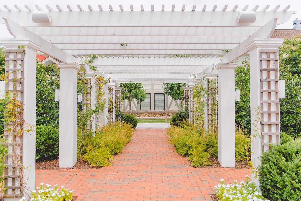 White garden pergola over a brick walkway lined with greenery and blooming flowers in spring