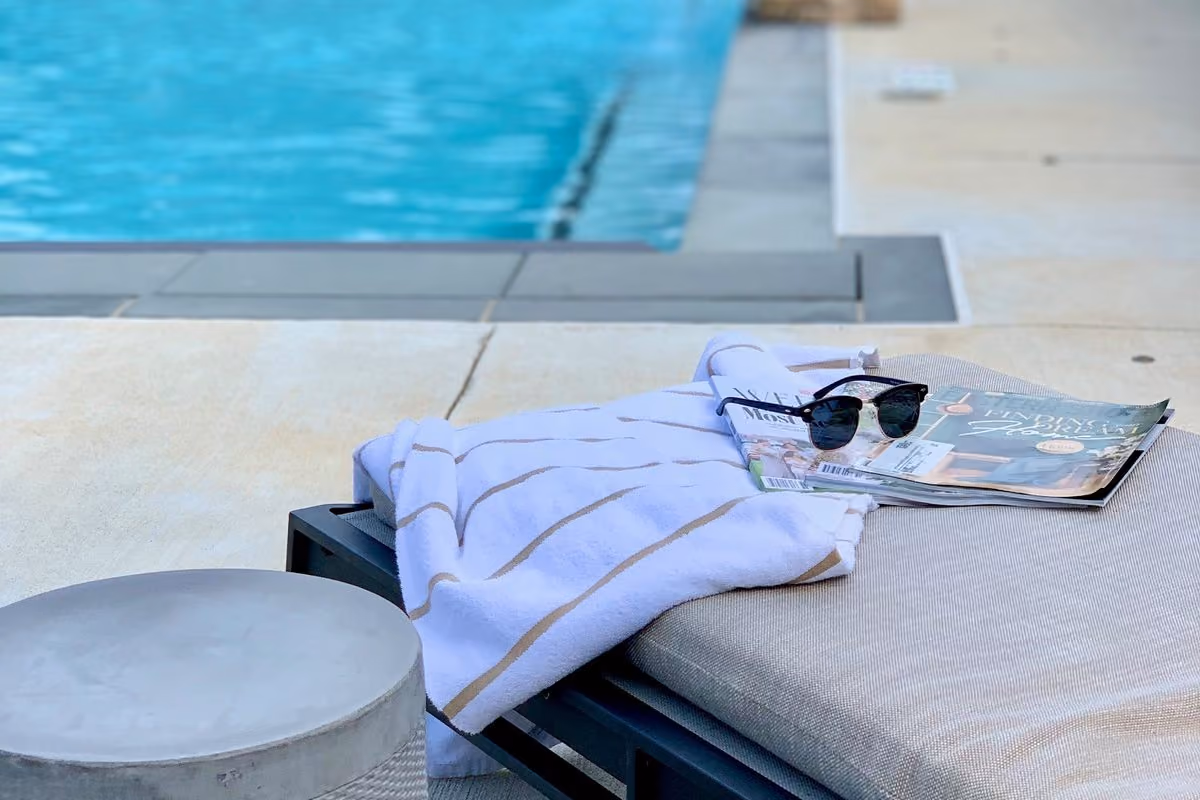Poolside lounge chair with a towel, sunglasses and a magazine beside the outdoor pool on a sunny day