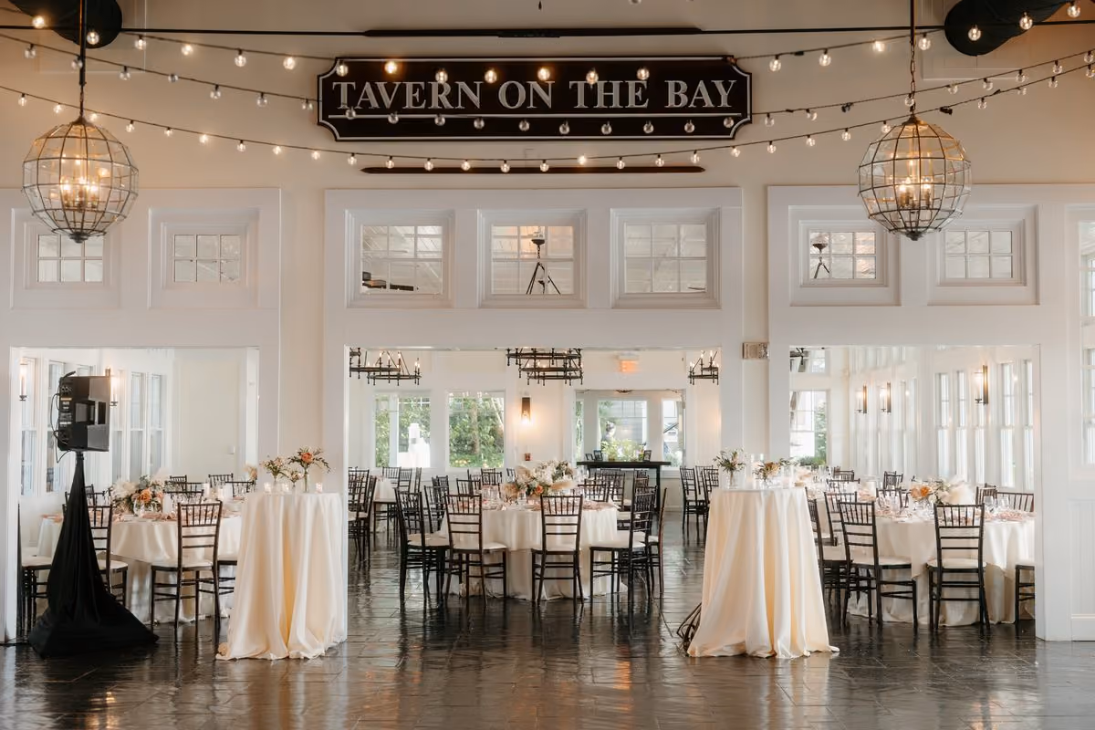 Tavern on the Bay reception space with string lights, globe chandeliers and round tables set for a wedding at Chesapeake Bay Beach Club