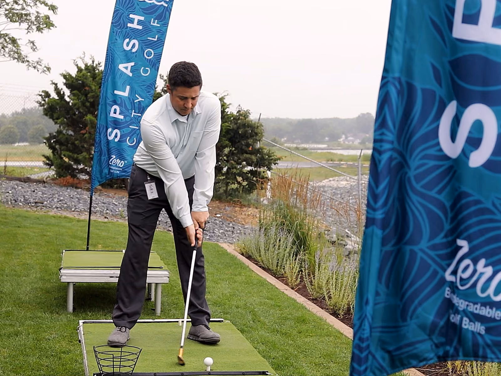 Guest driving golf balls at a Splash City Golf team-building activity on the waterfront lawn