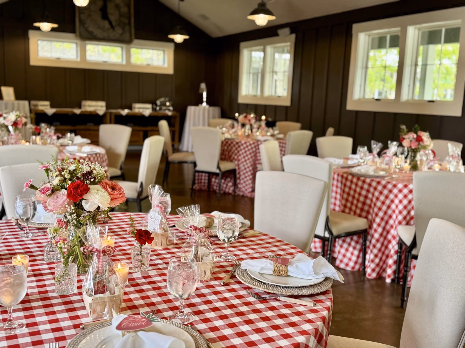 Rustic private event room with red gingham linens, white chairs and floral centerpieces set for a themed gathering
