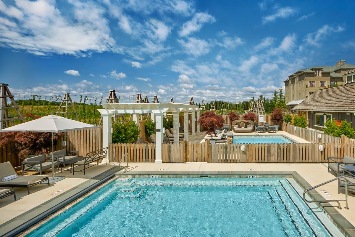 Outdoor resort pools with a pergola, lounge chairs and umbrellas under a blue sky for a spa pool pass