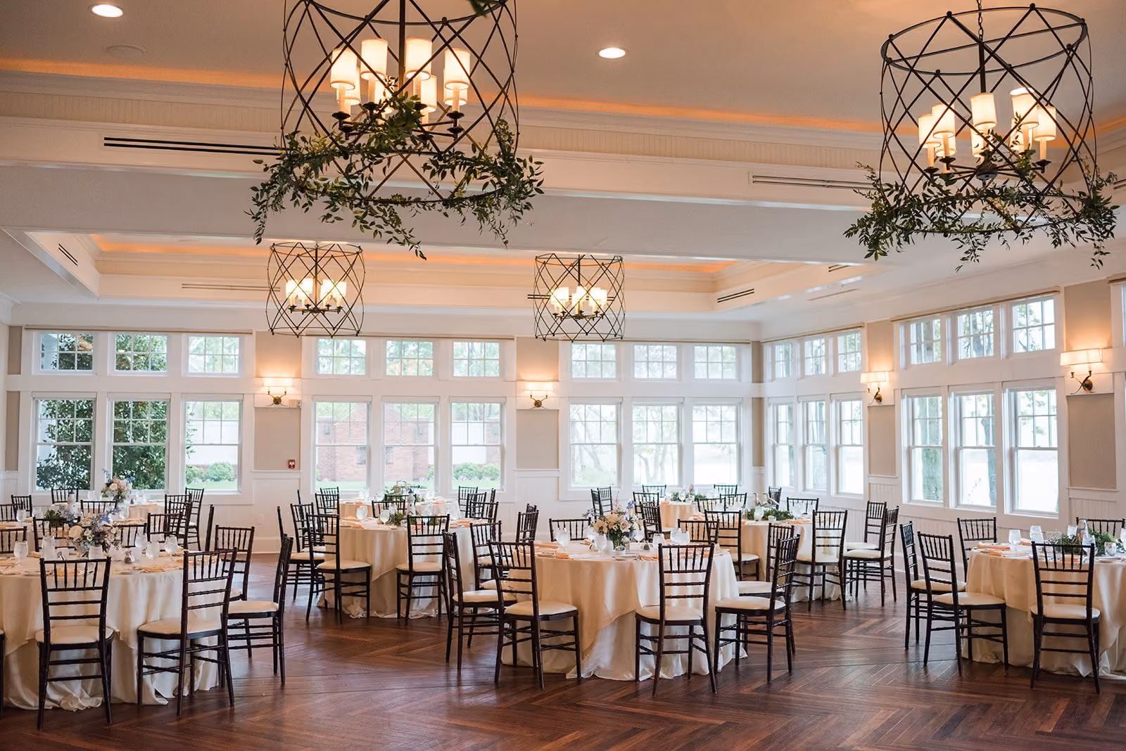 Evening reception in the Sunset Ballroom with greenery-wrapped iron chandeliers and round tables at Chesapeake Bay Beach Club