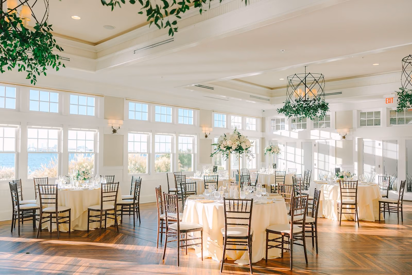Sunset Ballroom reception with hanging greenery chandeliers and bay-view windows at Chesapeake Bay Beach Club