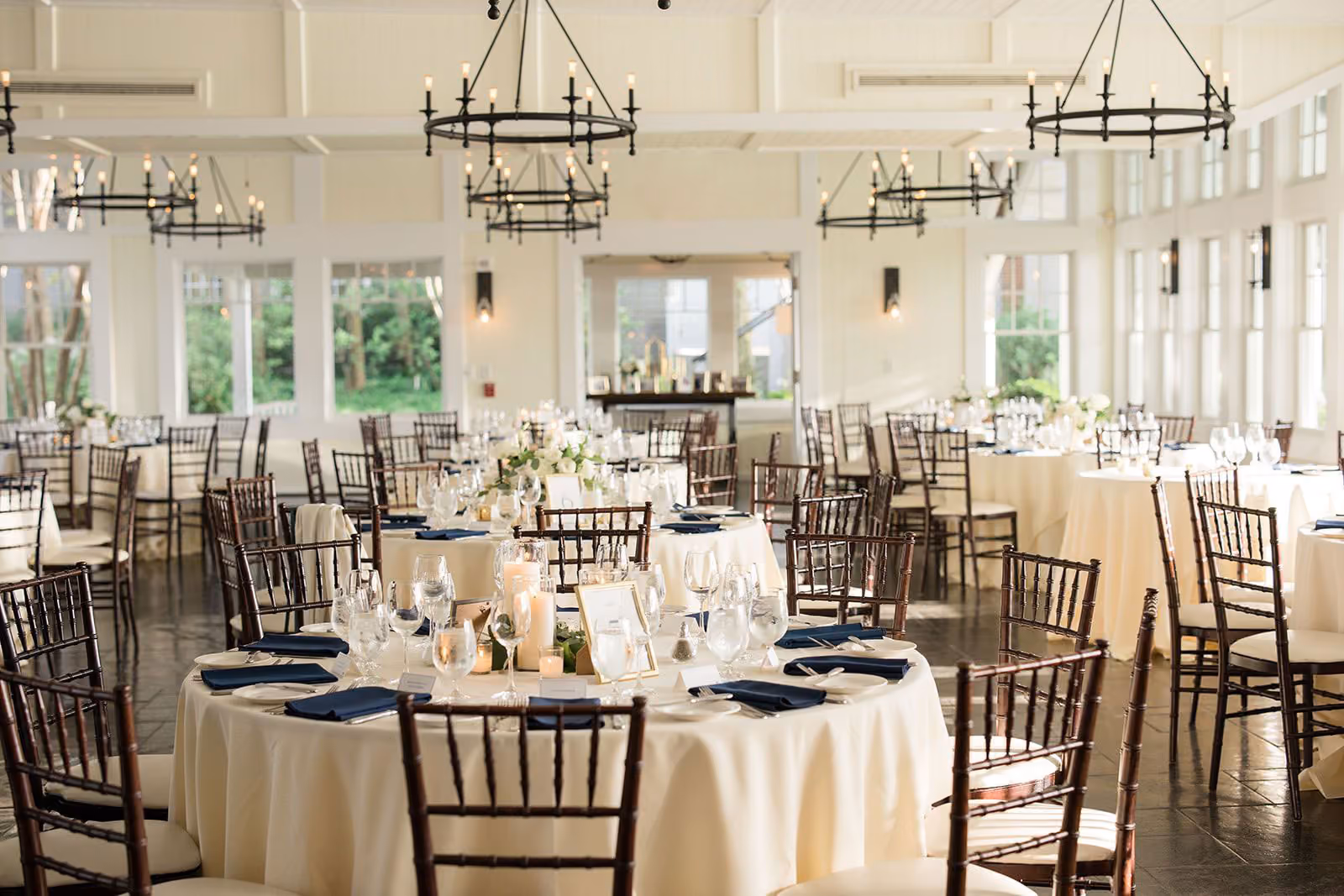 Tavern Ballroom set for an event with round tables, greenery, and bay-view windows at Chesapeake Bay Beach Club