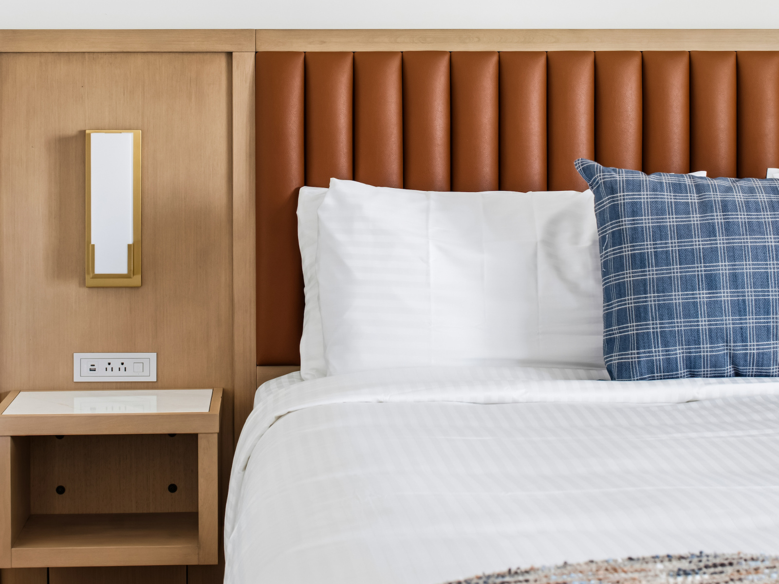 King bed at Wilson’s Cove featuring a warm wood headboard, leather detailing and coastal blue accents.