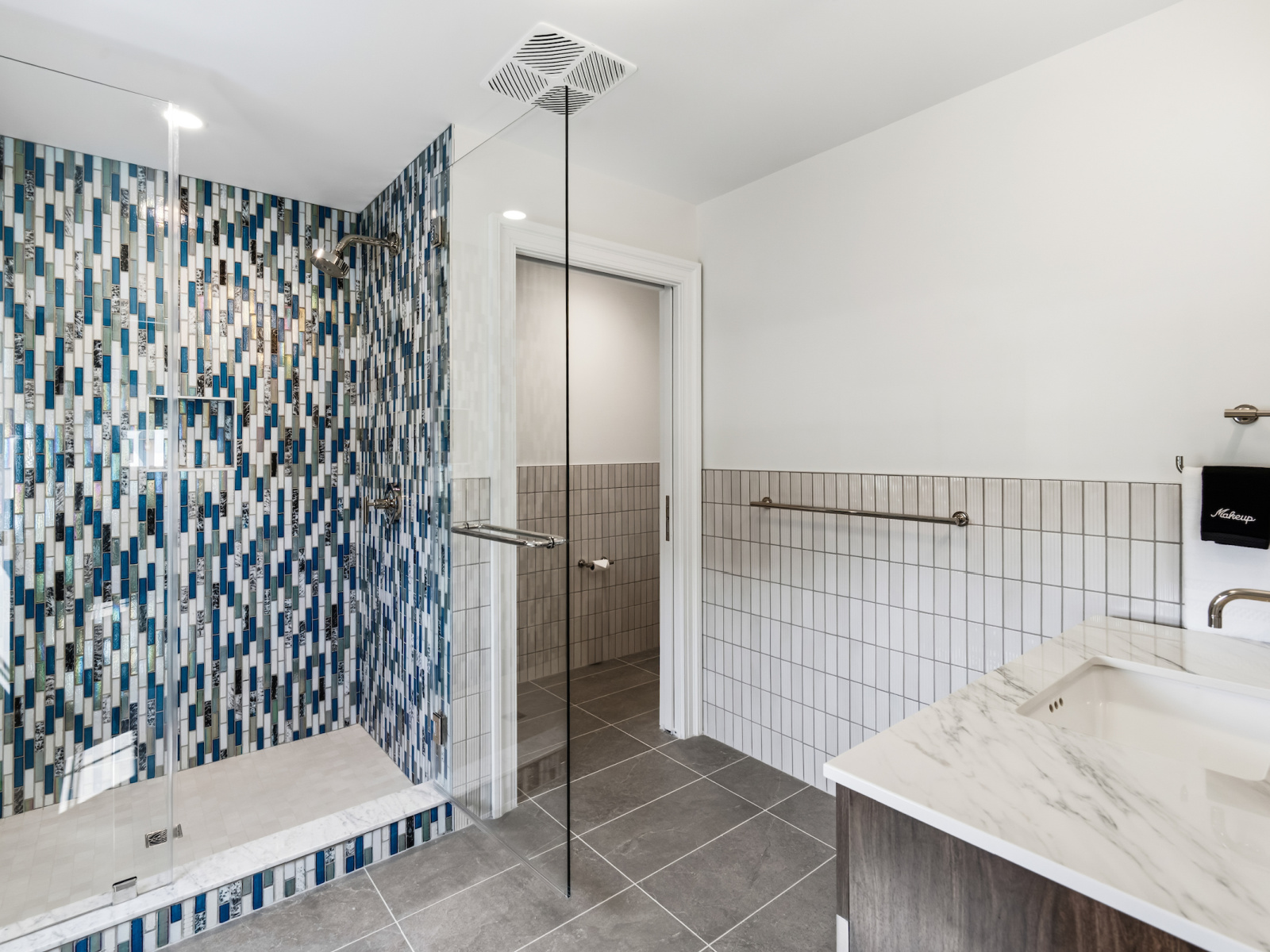 Mariner Suite bathroom at Wilson’s Cove featuring an accessible walk-in shower with blue mosaic tile and marble-top vanity.