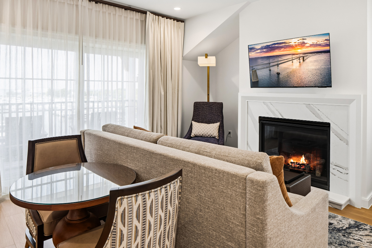 Modern hotel room with a large bed, two chairs, desk, and balcony overlooking a sunset view through sliding glass doors.