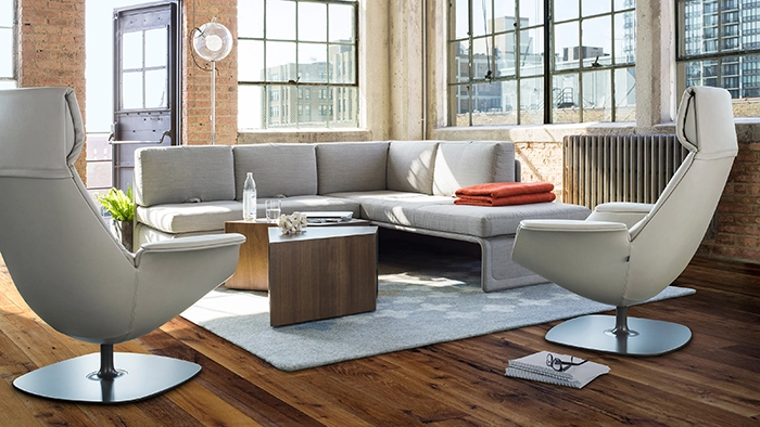 Modern office lounge seating area with sofas and swivel chairs around a coffee table in a bright, open workspace