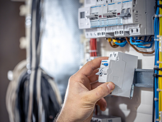 Électricien installant un disjoncteur dans un tableau électrique avec câbles colorés.