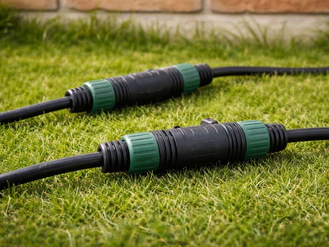 Raccords électriques étanches noirs et verts connectant des câbles posés sur une pelouse.