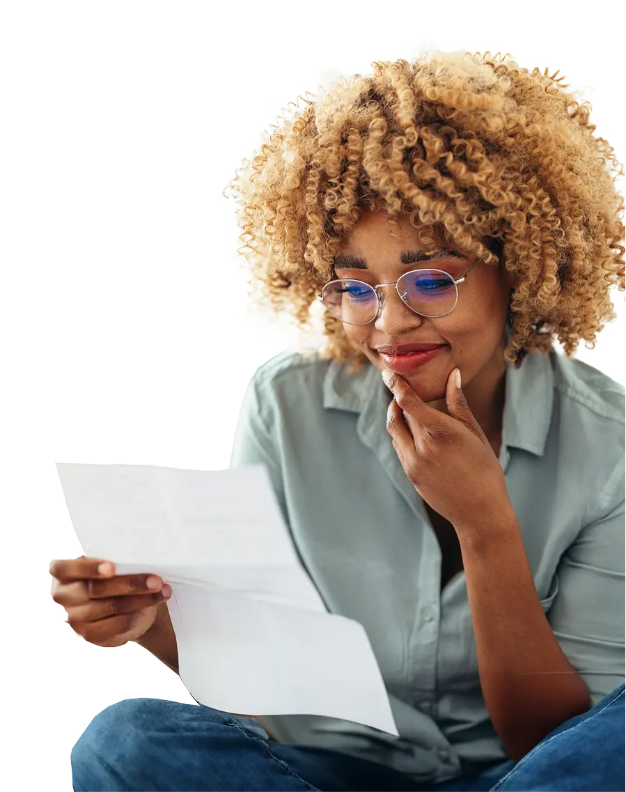 Young woman with curly hair and glasses reading a paper with a slight smile and thoughtful expression.