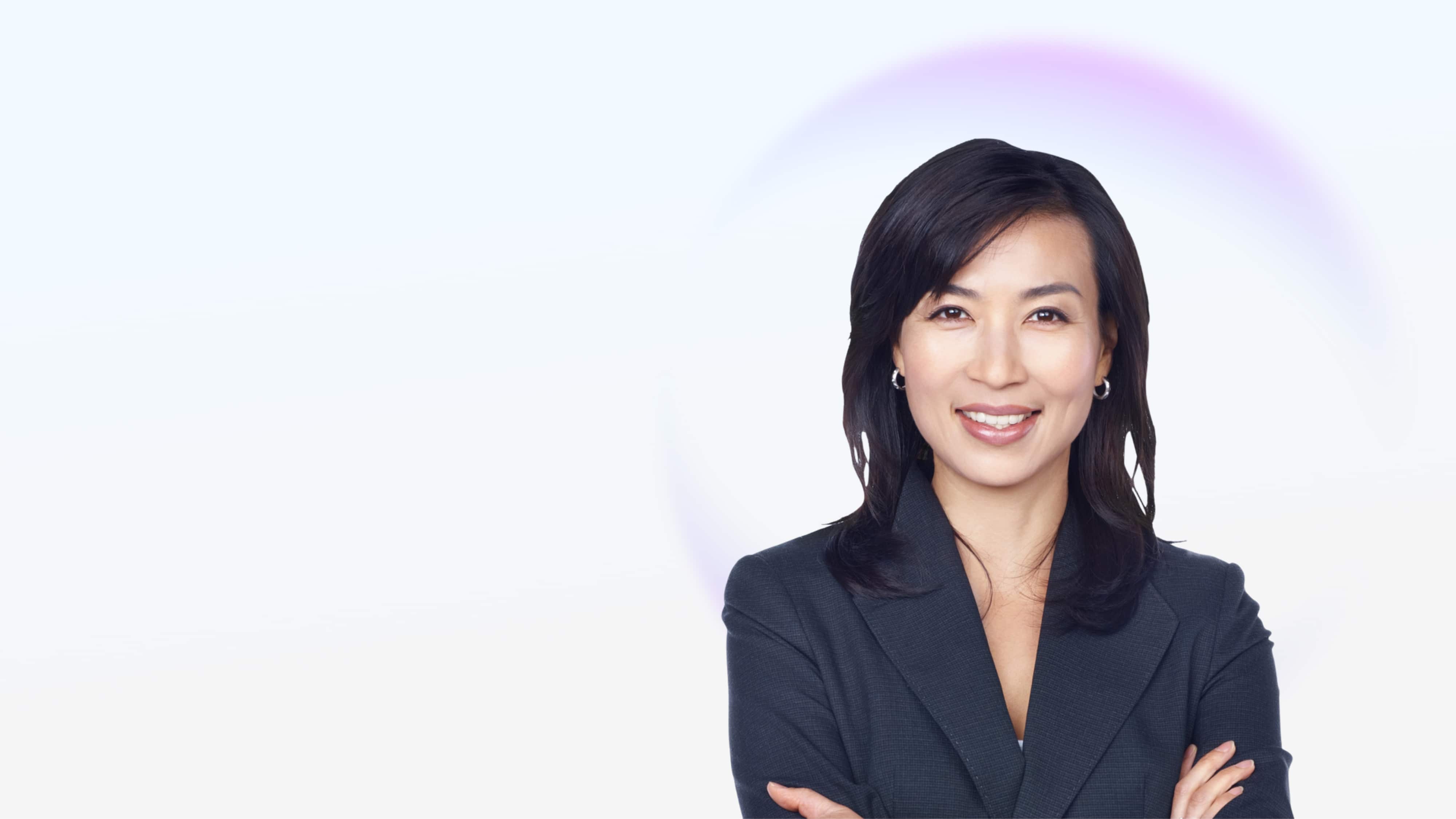 Smiling businesswoman with dark hair wearing a dark blazer, arms crossed, on a light background.