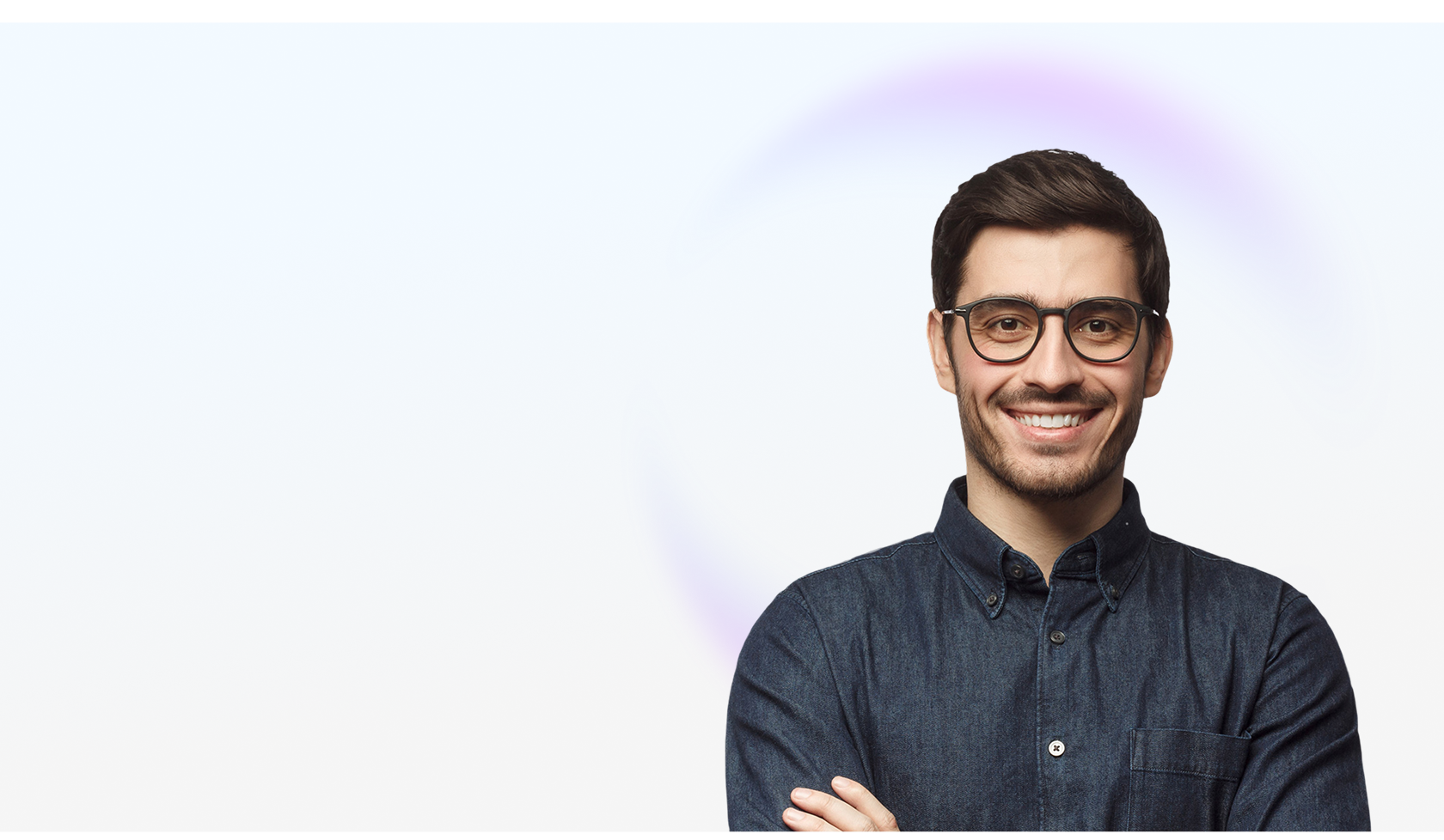 Smiling man with glasses and dark denim shirt standing with arms crossed on light background.