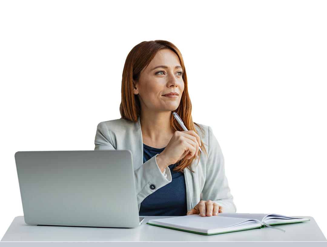 Woman with red hair holding a pen and looking away, sitting at a desk with laptop and open notebook.
