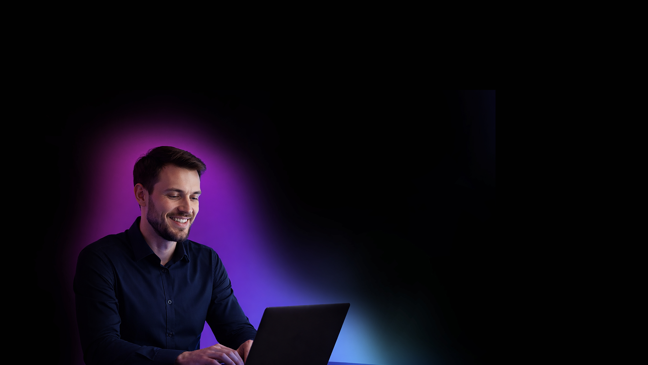 Smiling man in dark shirt working on a laptop with purple and blue glow on a black background.